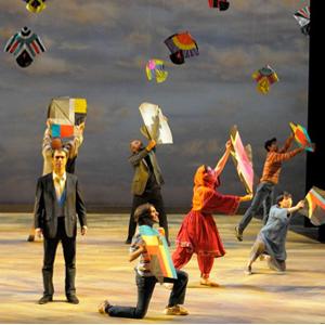 Actors on stage pose in various ways while flying colorful kites in the air.