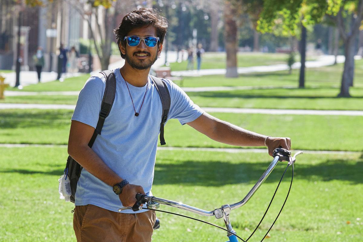 Student wearing shades holding up a cruiser bike.