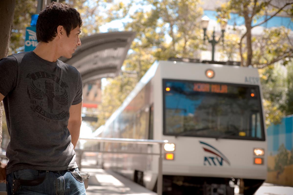 A student looking back at the approaching VTA light rail on a sunny day.