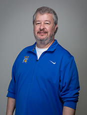 waist-up photo of John Gibbs, Caucasian Male with short gray hair and short beard, wearing blue Spartan track jacket with a white undershirt